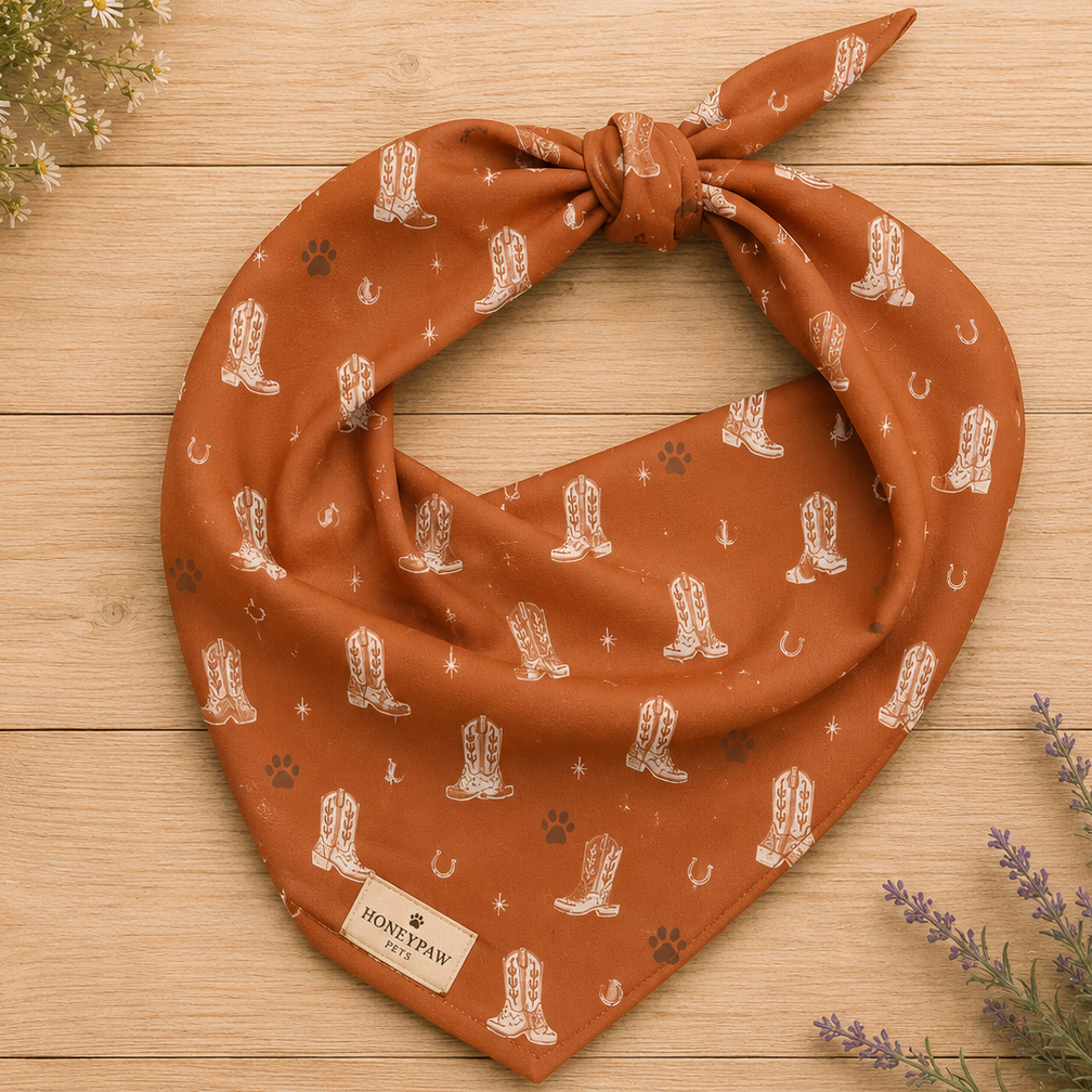 Display photo of a orange cowboy boot HoneyPaw Pets dog bandana on a wood background