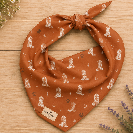 Display photo of a orange cowboy boot HoneyPaw Pets dog bandana on a wood background