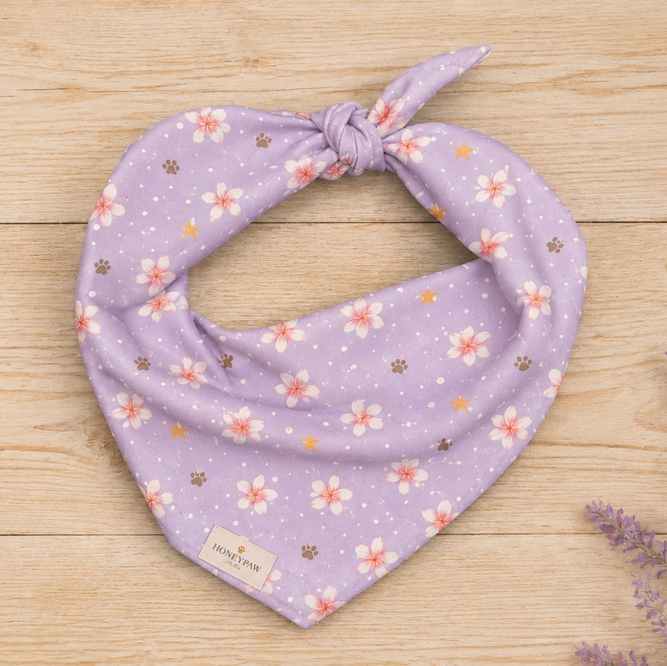 Island Scent dog bandana featuring pink plumeria flowers, paw prints, and golden stars on a lavender background by HoneyPaw Pets.